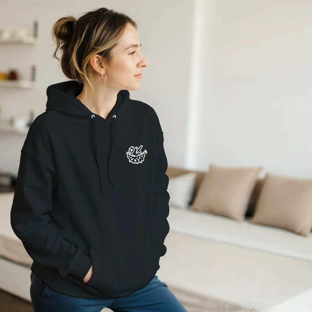 Person wearing a black hoodie with a logo in a room with a couch and pillows. Drum and bass