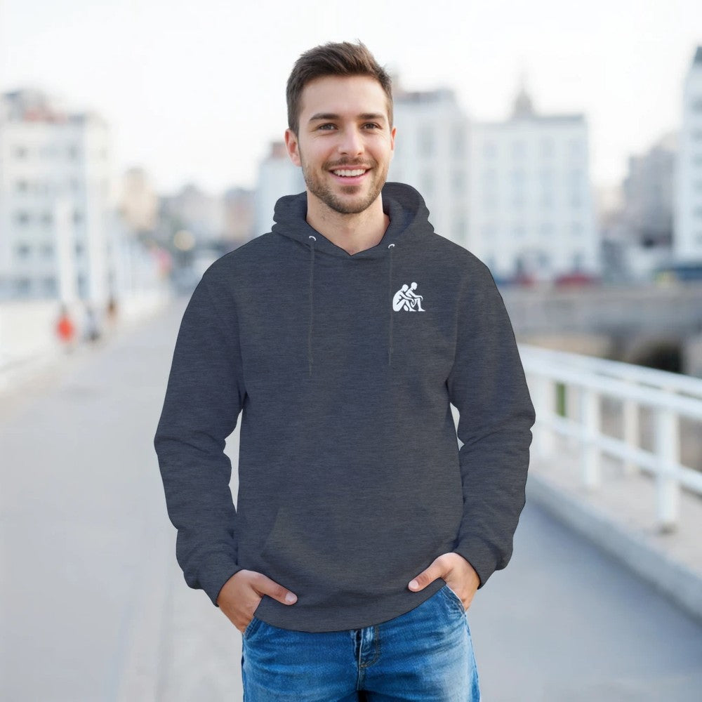 Man wearing a dark gray hoodie with a logo, standing outdoors with a blurred cityscape background.