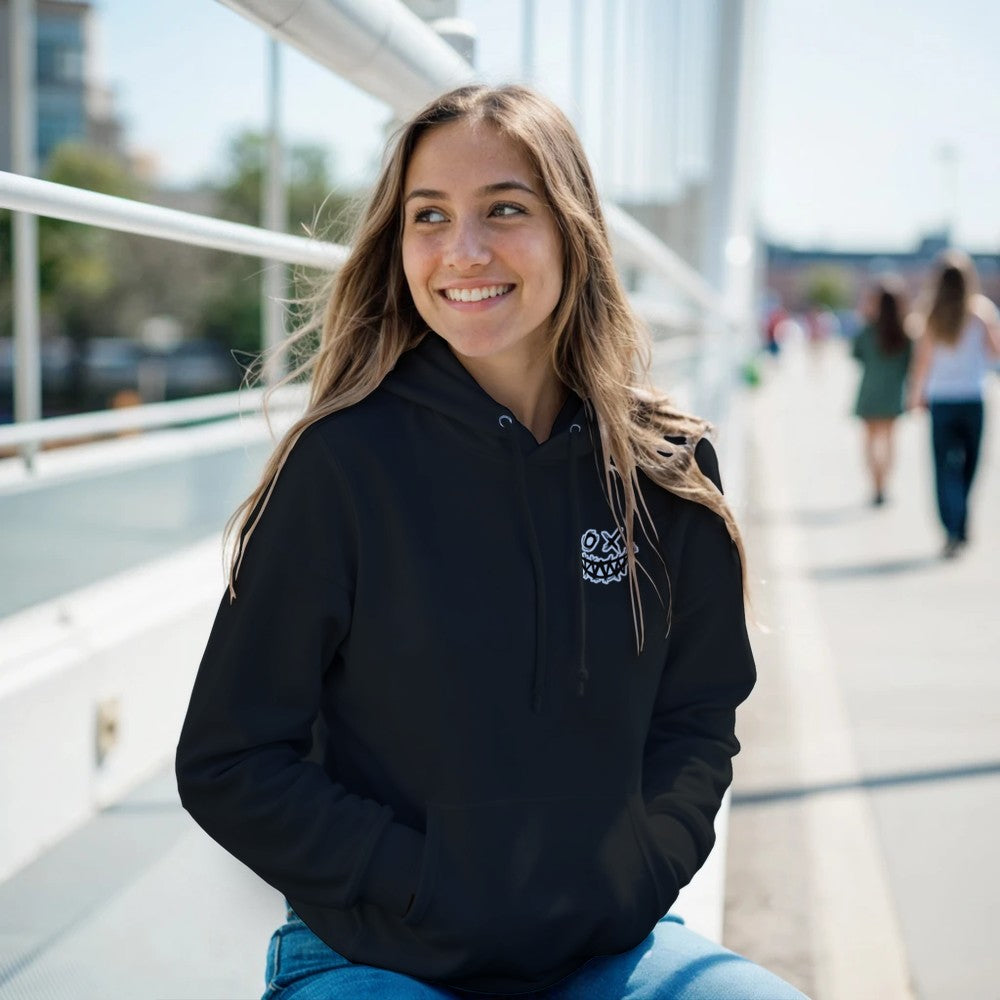 Woman wearing a black hoodie with a logo, sitting outdoors on a sunny day. Drum and bass
